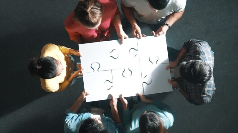 Top down view of business people gathering jigsaw together at meeting. Aerial view of diverse team collect or put piece of jigsaw puzzle together and standing while wearing casual cloth. Symposium.
