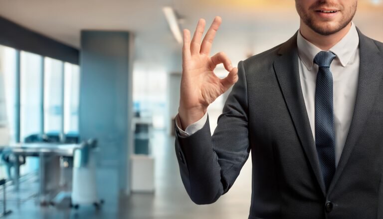 Businessman in a suit gives the OK sign in a modern office, signaling success, approval, and positive agreement.